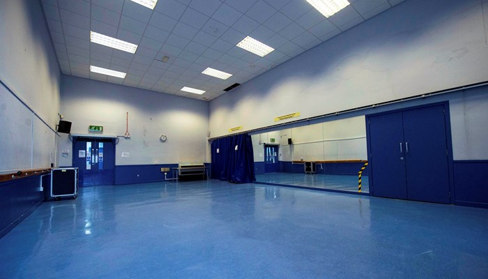 large empty room with blue floor and white ceiling and walls. there is a mirror across the furthest wall