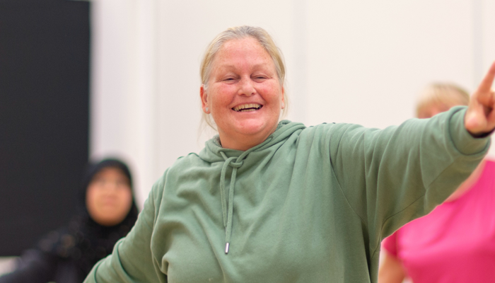 A person smiling during a wellbeing class with their left hand in the air pointing