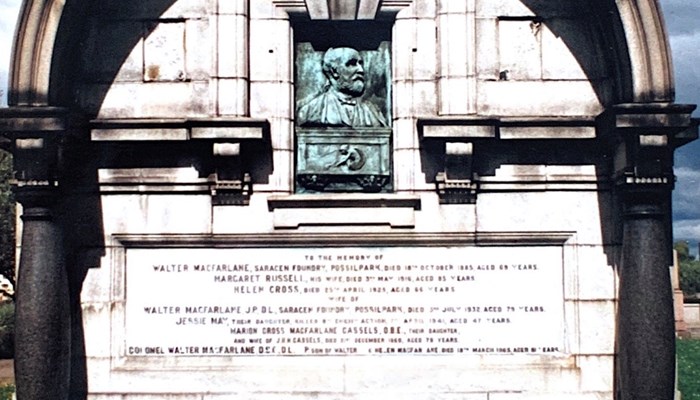 A photograph of a large memorial for Walter MacFarlane which has pillars holding an arch up over a face that has oxidised and turned turquoise. 