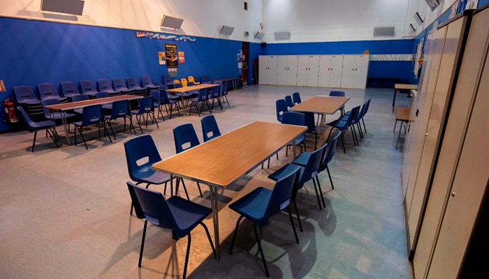 large room with multiple wooden tables and blue chairs placed around the room. there are lockers on the far wall and the wall on the right hand side of the room