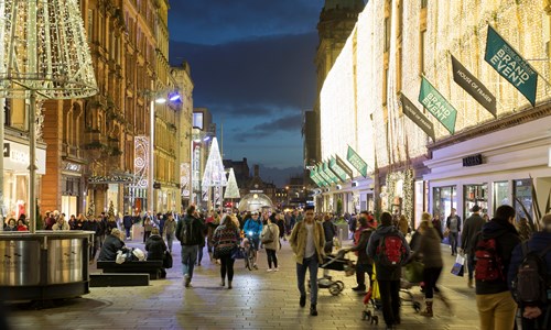 Shoppers walking up Buchanan Street with festive lights in the background 