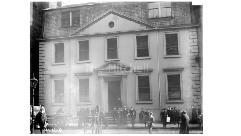 black and white photograph of a two storey building with 5 windows along the upper storey and a large entrance doorway centred on the ground floor