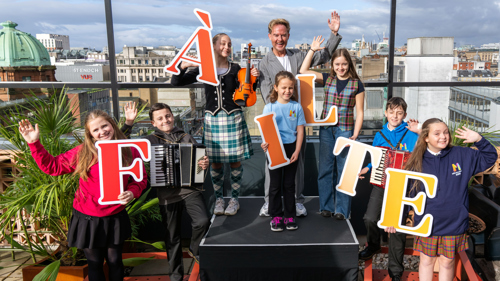 Children and a man stand on a rooftop in front of railings holding letters which spell out the word 'failte'