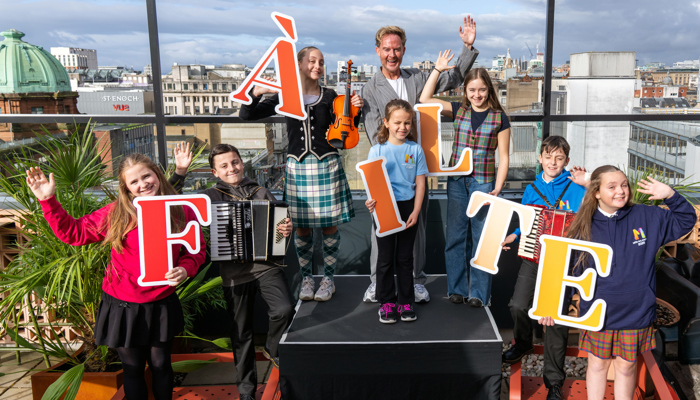 Children and a man stand on a rooftop in front of railings holding letters which spell out the word 'failte'