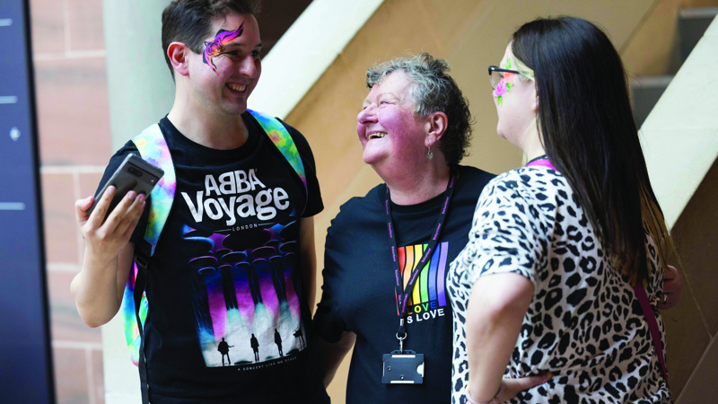 Three people with colourful face paint chatting together at a community event indoors.