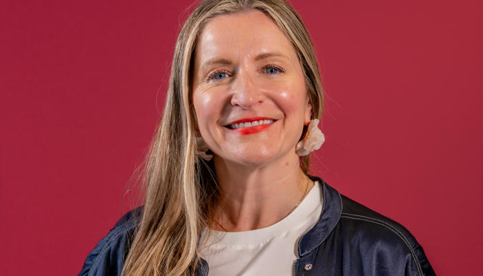 A woman with light brown hair smiles in front of a rubine background