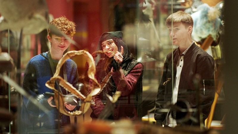 A group of three young people looking at objects in a glass display case in Kelvingrove Art Gallery and Museum