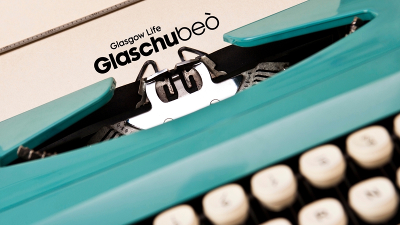 A finger hovers over an old-fashioned typewriter. A Gaelic Glasgow Life logo sits at the top of the paper in it