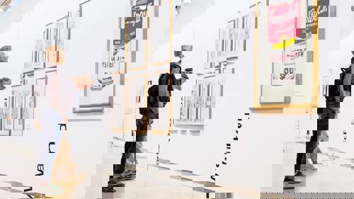 Photograph of two people looking at framed prints on the wall at GoMA