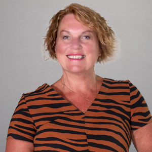 A headshot of Jan Buchanan, wearing an organge and black striped top. 