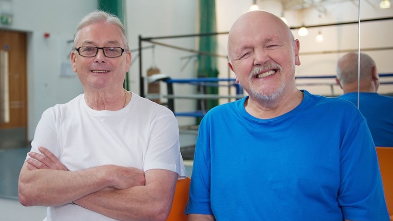 Two men sitting next to each other and smiling in a boxing gym