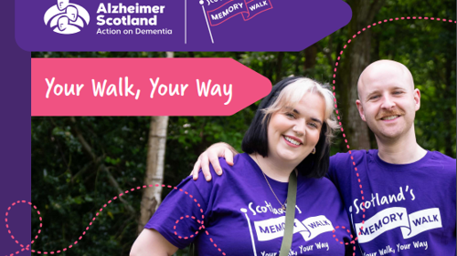 Two people wearing the same purple t-shirts that read Memory Walk are standing next to each other smiling in a wooded area of a park